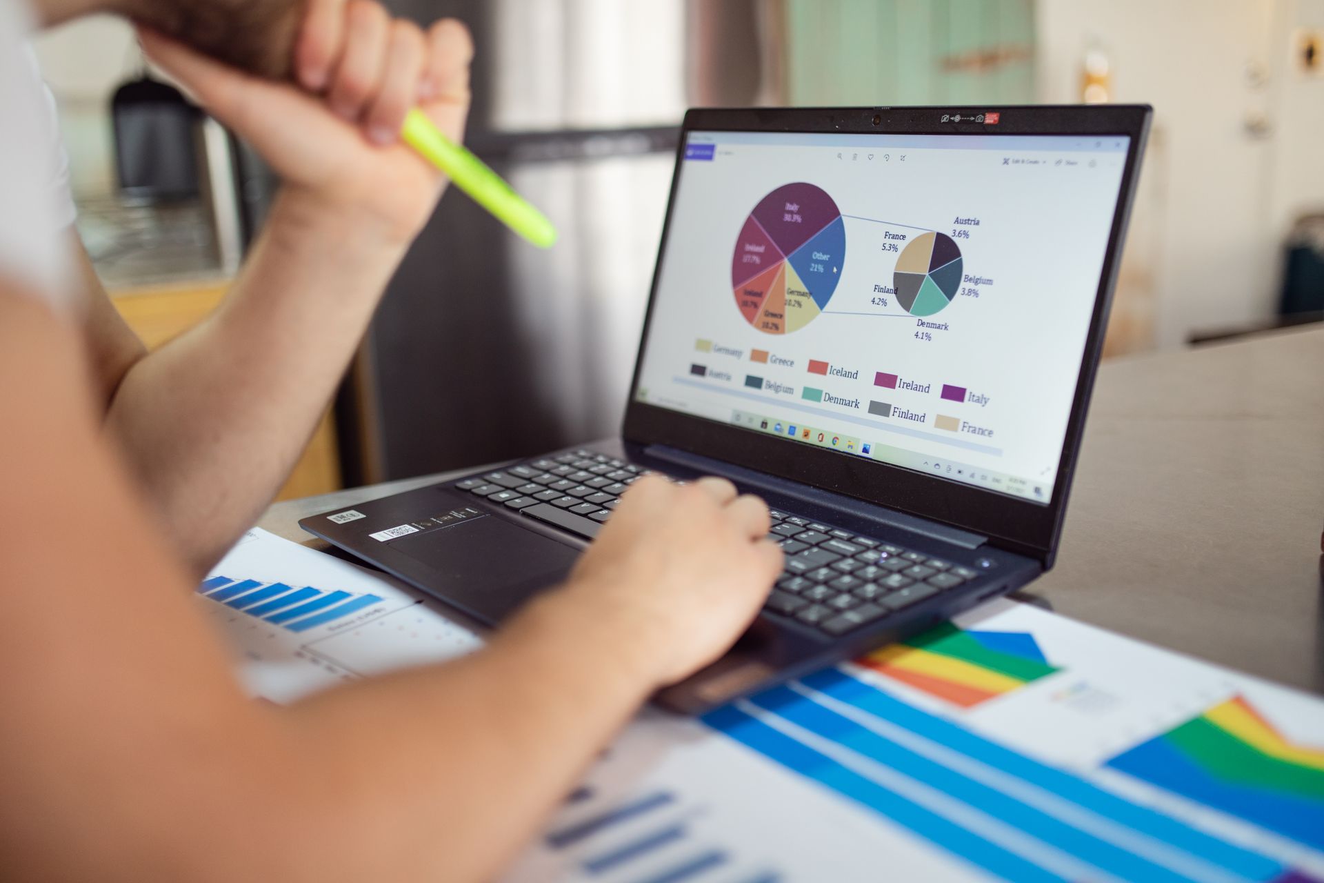 Someone reviewing sales charts on a laptop beside printed reports